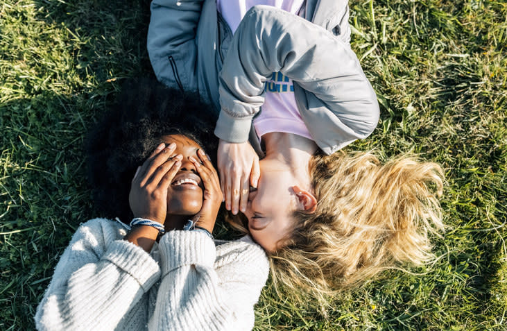 two girls lying in the grass with their heads next to each other laughing