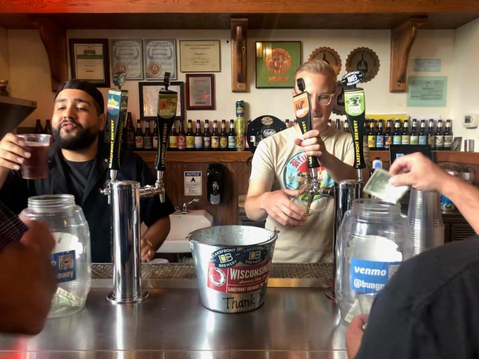 Lakefront Brewery tour guide Serg left, and a Lakefront bartender pour beers in the middle of a Lakefront Brewery tour on July 6, 2023.