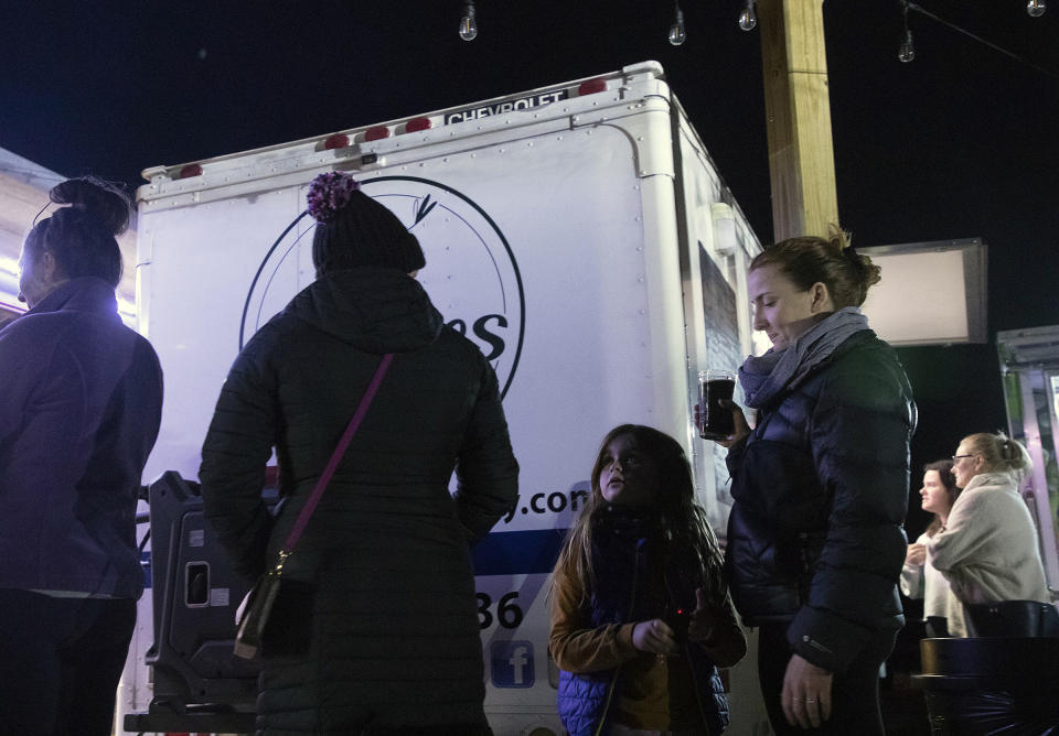 Elowyn Hoelscher, 7, stands in line at a food truck with her mother, Erika Hoelscher, at Red's Corner during the Moore County power outage on Monday, Dec. 5, 2022, in Southern Pines, N.C. Tens of thousands of people are bracing for days without electricity in Moore County where authorities say two power substations were shot up by one or more people with apparent criminal intent. (Kaitlin McKeown/The News & Observer via AP)