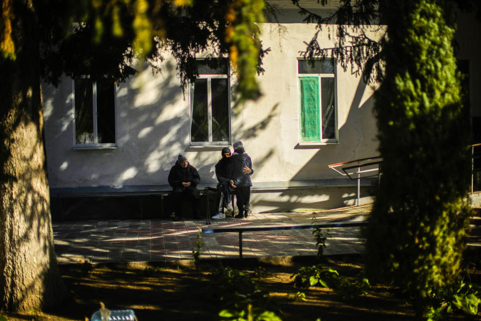 Bohdan, right, whose father Mykola Svyryd, 70, died several days before, is hugged by a resident in a shelter for injured and homeless people in Izium, Ukraine, Wednesday, Oct. 12, 2022. A young Ukrainian boy with disabilities, 13-year-old Bohdan, is now an orphan after his father, Mykola Svyryd, was taken by cancer in the devastated eastern city of Izium. (AP Photo/Francisco Seco)