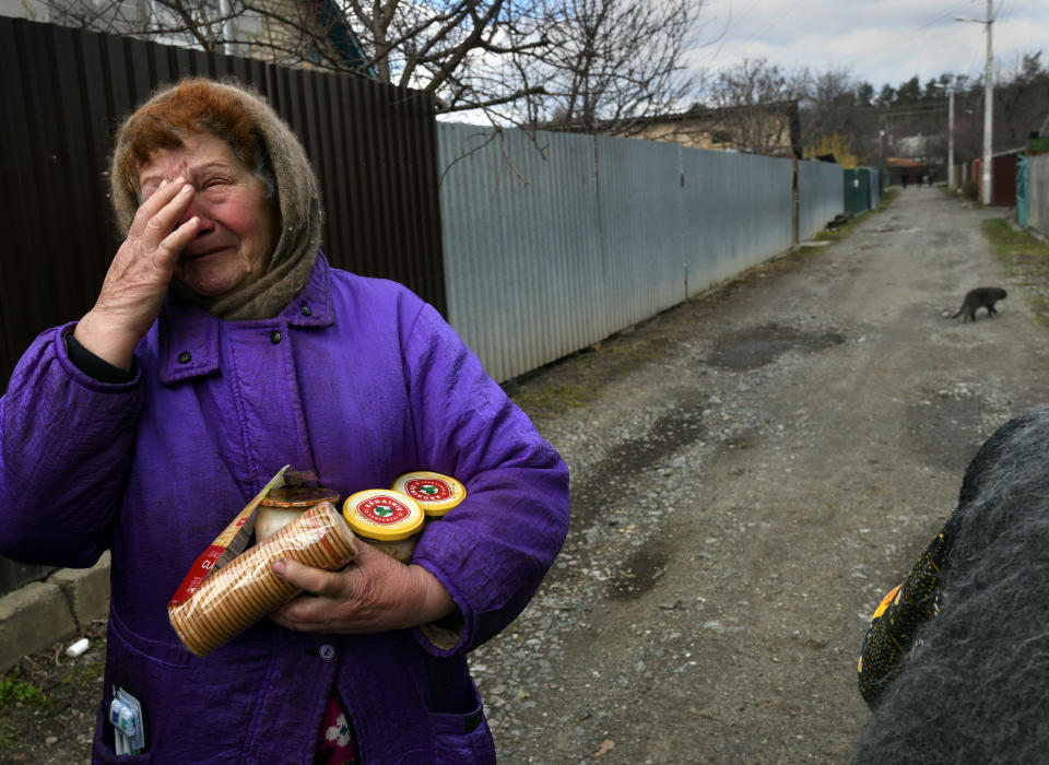 A distraught woman in a purple coat and wool headscarf carries food aid, including crackers, handed out in Bucha.