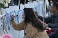 People write messages on wooden hearts displaying names of victims at a vigil outside Monterey Park City Hall, blocks from the Star Ballroom Dance Studio on Tuesday, Jan. 24, 2023, in Monterey Park, Calif. A gunman killed multiple people at the ballroom dance studio late Saturday amid Lunar New Years celebrations in the predominantly Asian American community. (AP Photo/Ashley Landis)