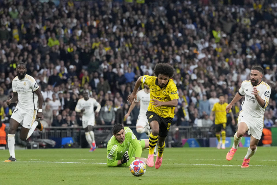 Karim Adeyemi (centro) del Borussia Dortmund se desmarca del arquero Thibaut Courtois (en el piso) del Real Madrid durante la final de la Liga de Campeones, el sábado 1 de junio de 2024, en Londres. (AP Foto/Frank Augstein)