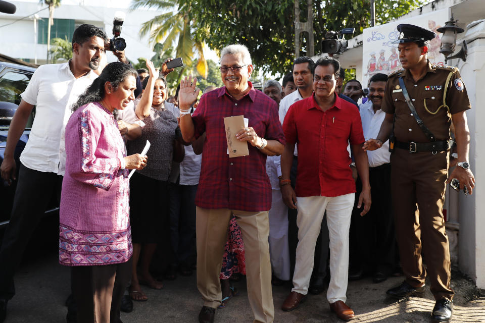 Sri Lanka's former Defense Secretary and presidential candidate Gotabaya Rajapaksa, center, waves to the media as he arrives to cast vote with his wife Ayoma, left, out side a polling center in Embuldeniya, on the outskirts of Colombo, Sri Lanka, Saturday, Nov. 16, 2019. Polls opened in Sri Lanka’s presidential election Saturday after weeks of campaigning that largely focused on national security and religious extremism in the backdrop of the deadly Islamic State-inspired suicide bomb attacks on Easter Sunday. (AP Photo/Eranga Jayawardena)