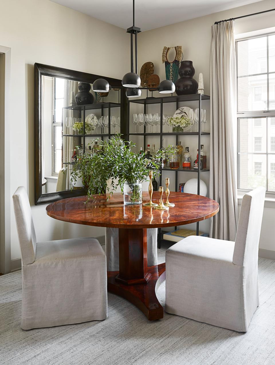 In the dining area, the designer has installed a chandelier from Capital Lighting. Dining chairs that the designer purchased at Clarke Auction Gallery sidle up with a vintage dining table, also purchased at auction. The candlesticks are by Eva Zeisel. Next to them, bar shelving—purchased at IKEA—displays a Roy Hamilton Studios vase and mementos Risdon bought during a trip to Indonesia.