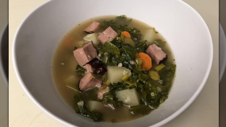 Ham and kale soup in white bowl 