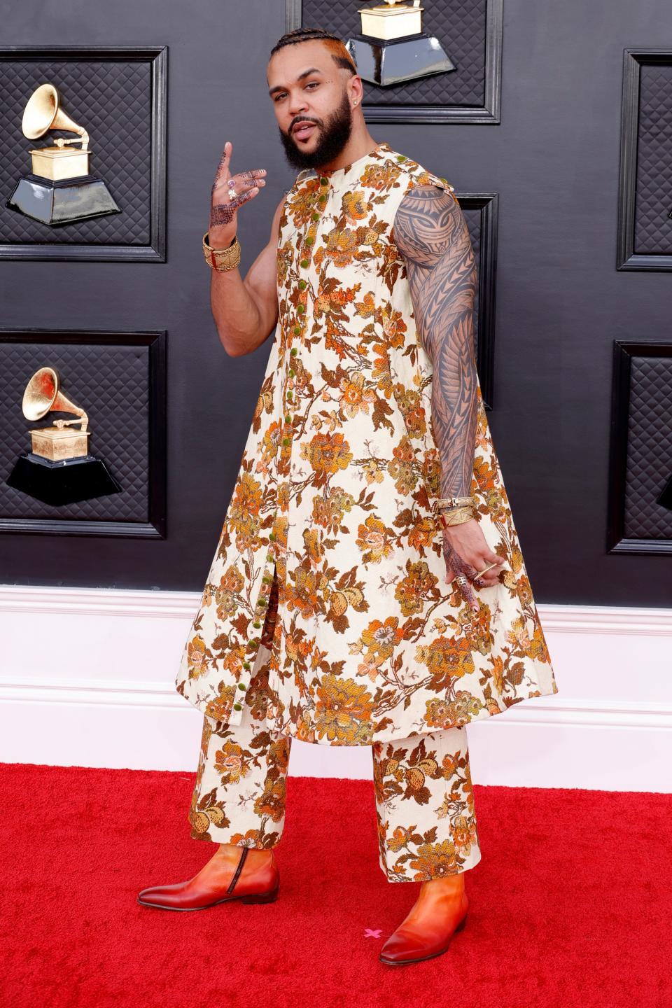 Jidenna in a beige flared dress tunic and matching pants with an orange floral print. He's wearing orange ombre boots.