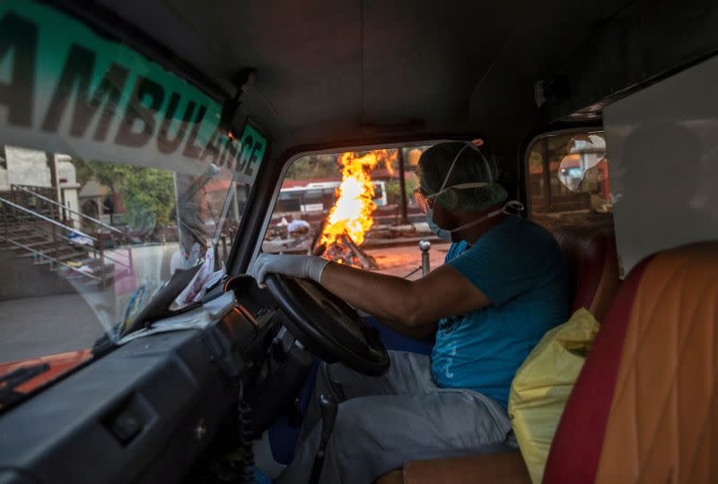 Mohammad Aamir Khan, an ambulance driver, drives past a pyre of a man who died due to the coronavirus disease, at a crematorium in New Delhi