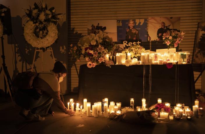 A masked person places a candle on the floor among others in a vigil