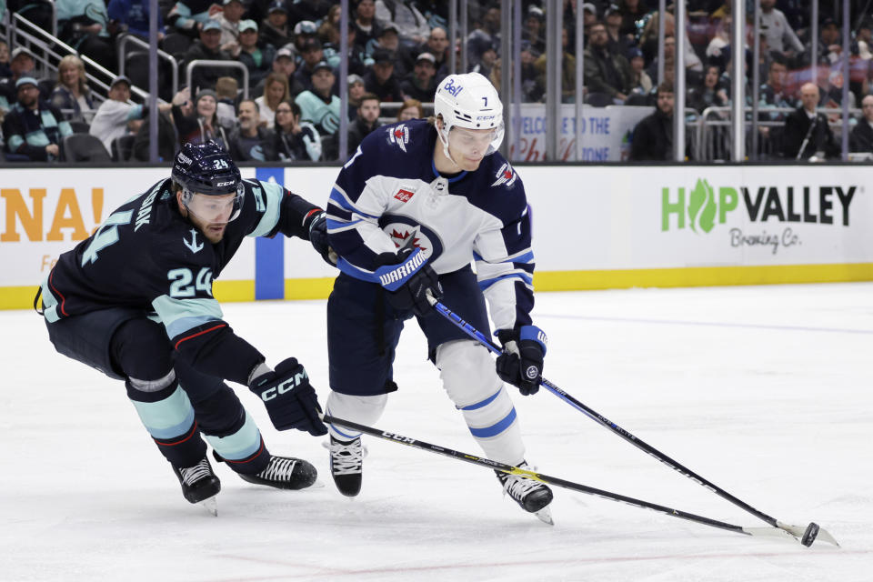 Winnipeg Jets center Vladislav Namestnikov (7) controls the puck under pressure from Seattle Kraken defenseman Jamie Oleksiak (24) during the second period of an NHL hockey game, Friday, March 8, 2024, in Seattle. (AP Photo/John Froschauer)