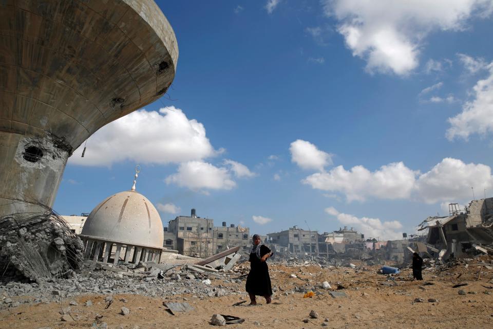 Palestinian women walk past a mosque and water tower damaged by what police said were Israeli air strikes and shelling in Khuzaa, east of Khan Younis, in the southern Gaza Strip August 3, 2014