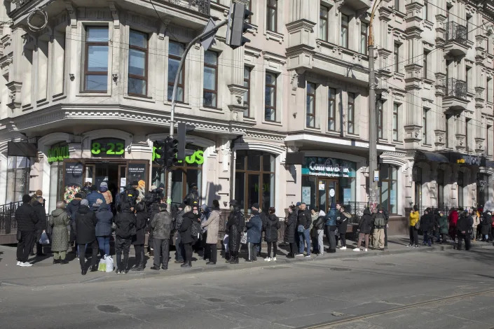 A line of people snakes around a building as they wait to enter a grocery store. 