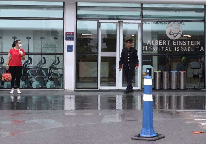 A woman wearing a protective mask stands in front Albert Einstein Hospital in Sao Paulo