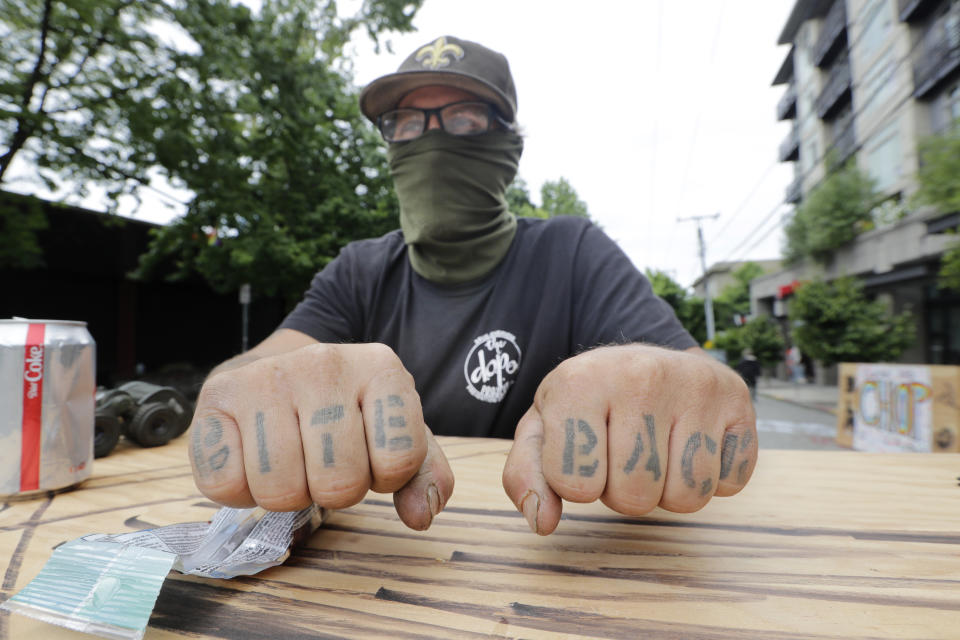 Michael, who declined to give his last name, displays his "bite back" tattoos as he stands guard to help keep peace Sunday, June 21, 2020, in Seattle, where streets are blocked off in what has been named the Capitol Hill Occupied Protest zone. Police pulled back from several blocks of the city's Capitol Hill neighborhood near the Police Department's East Precinct building earlier in the month after clashes with people protesting the death of George Floyd. (AP Photo/Elaine Thompson)