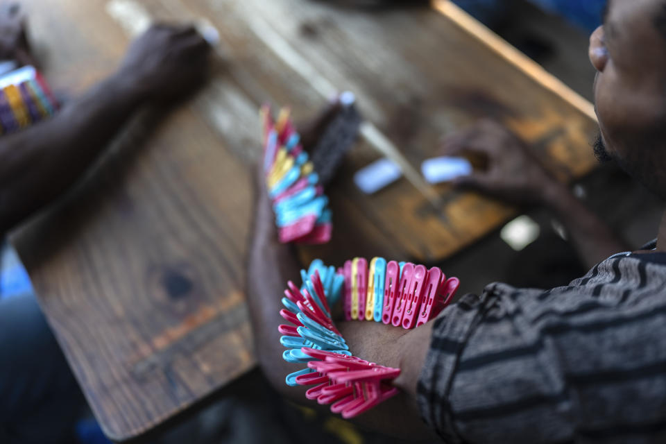 Clothespins pinch the arm of a domino player, each pin symbolizing when he loses, at a public school that serves as a shelter for people displaced from their homes due to clashes between armed gangs, in Port-au-Prince, Haiti, April 22, 2024. (AP Photo/Ramon Espinosa)