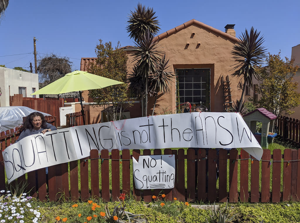 A Los Angeles resident sets a banner on her home fence reading “Squatting is not the Answer,” across the street of a formerly vacant home that had been recently taken over by a group of homeless mothers in 2020.