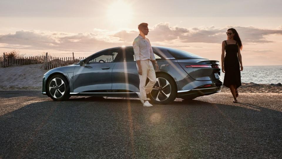 a man and woman standing next to a car on a road by the water