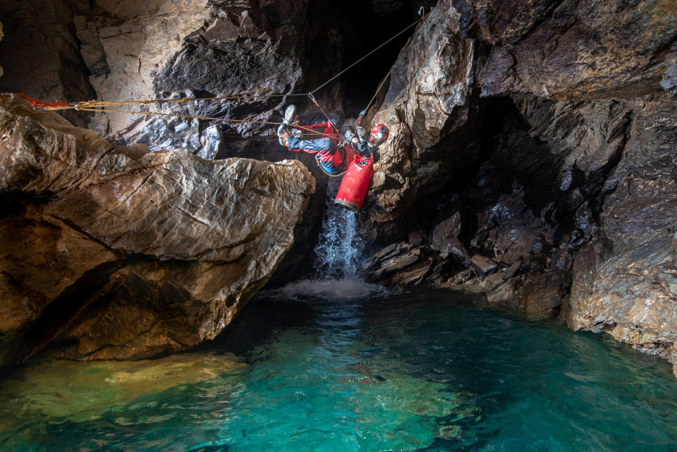 A caver attached to a rope climbing across a pool