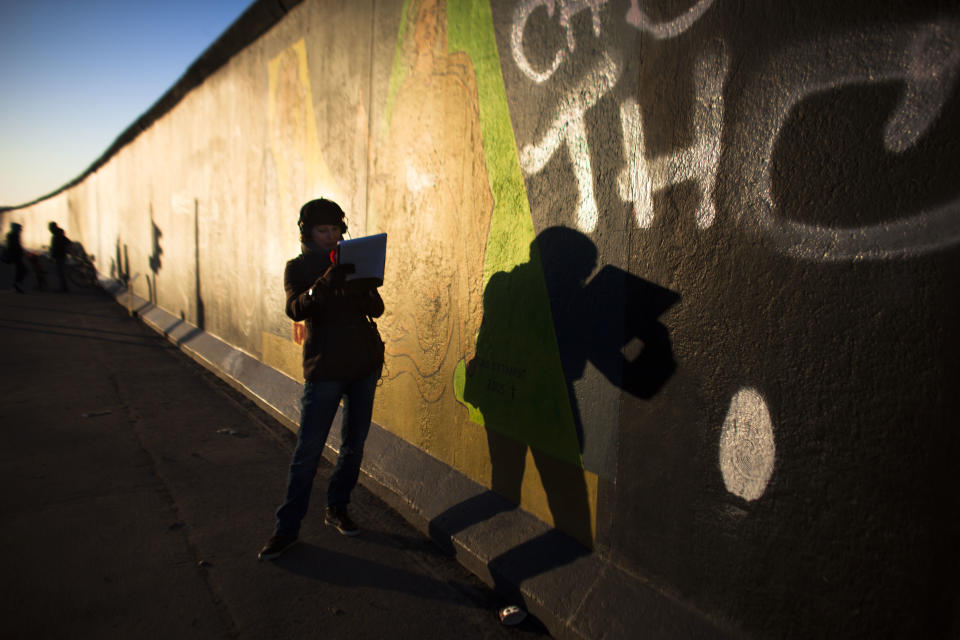 In early morning light, a radio broadcast journalist casts her shadow on the East Side Gallery named part of the former Berlin Wall as she reports about protests in Berlin, Monday, March 4, 2013. After massive protest over the last days an investor suspended the removal of a section of the historic stretch of the Berlin Wall known as the East Side Gallery to provide access to a riverside plot where luxury condominiums are being built. (AP Photo/Markus Schreiber)