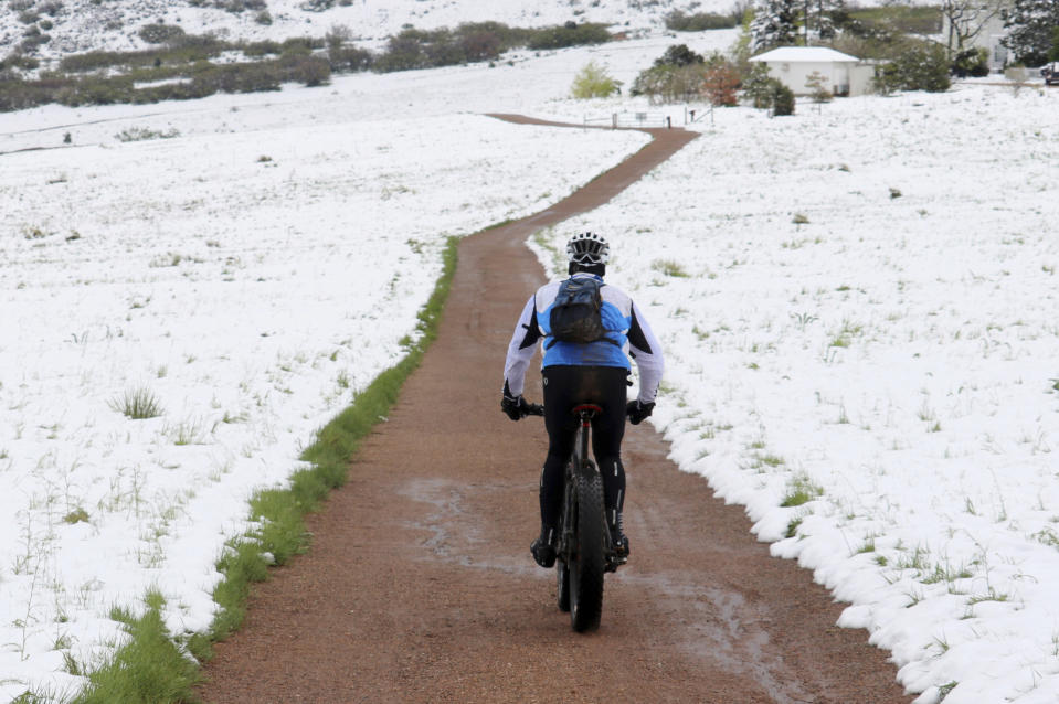 In this photo provided by Adriana Wiersma, a bicyclist rides a trail in the snow-covered Ken Caryl Valley near Littleton, Colo., after a late spring storm blanketed the area with snow, seen Tuesday morning, May 21, 2019. Much of the West is experiencing weird weather. Colorado and Wyoming got an unusually late dump of snow this week. In California, growers are frustrated by an unusually wet spring that has delayed the planting of some crops like rice and damaged others including strawberries and wine grapes. (Adriana Wiersma via AP)