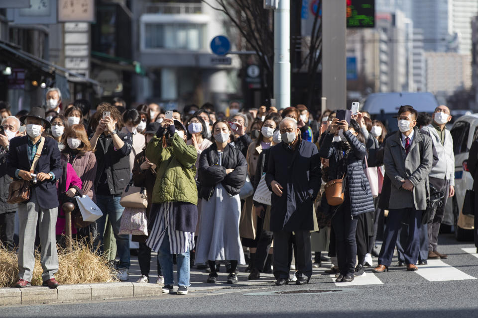 Some of the bystanders waiting at a traffic intersection take pictures of a clock on a building when the 10th annual tribute started at 2:46 p.m. for the victims of a 2011 disaster in Tokyo Thursday, March 11, 2021. Japan is marking the 10th anniversary Thursday of the earthquake, tsunami and nuclear disaster that hit the northeastern region. (AP Photo/Hiro Komae)