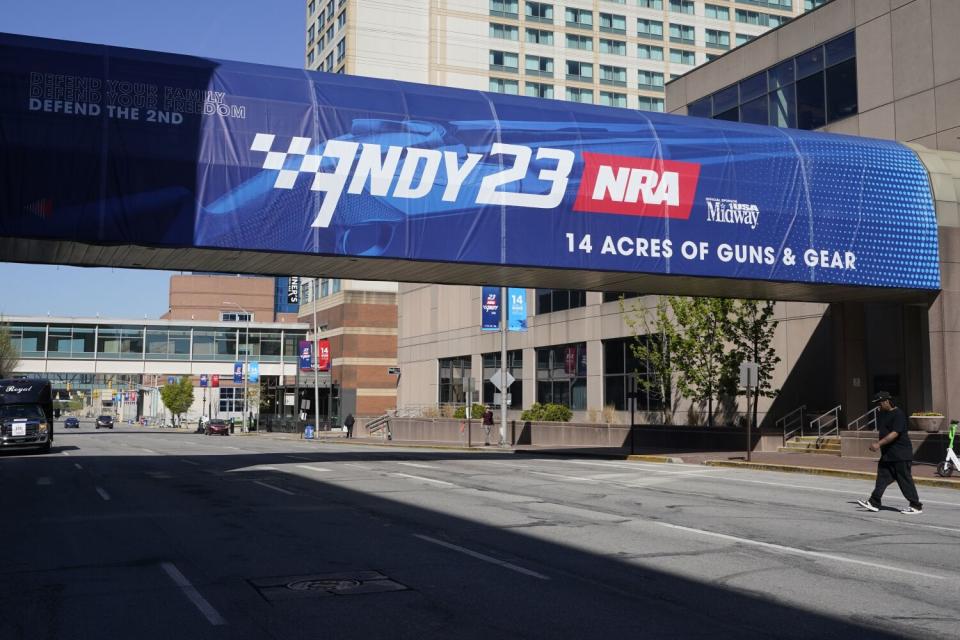 A pedestrian walks under a sign advertising the NRA convention in Indianapolis.