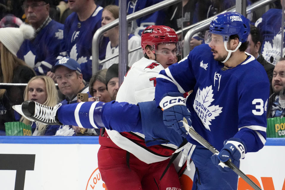 Carolina Hurricanes defenseman Dmitry Orlov (7) and Toronto Maple Leafs center Auston Matthews (34) go to the boards during third-period NHL hockey game action in Toronto, Saturday, Dec. 30, 2023. (Frank Gunn/The Canadian Press via AP)