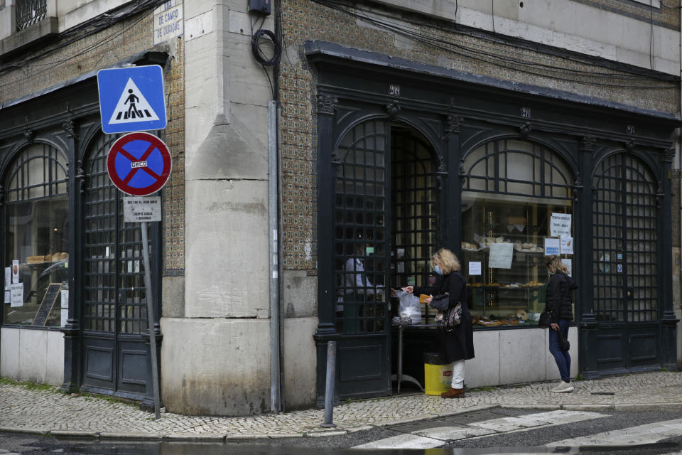 A woman buys food at the door of a pastry shop in Lisbon, Wednesday, Jan. 20, 2021. The pandemic has gained momentum in Portugal since Christmas, when restrictions on gatherings and movement were eased for four days. Restaurants and cafes are only allowed to serve food for takeaway. (AP Photo/Armando Franca)