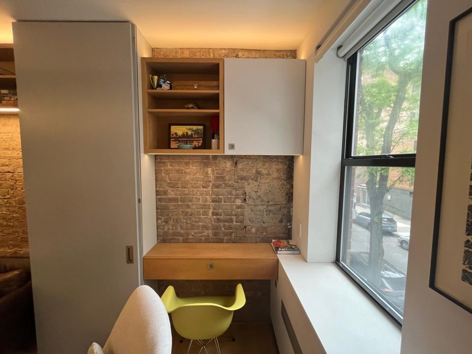 A corner of the living room with a cabinet above a small wooden desk with a patch of exposed brick.