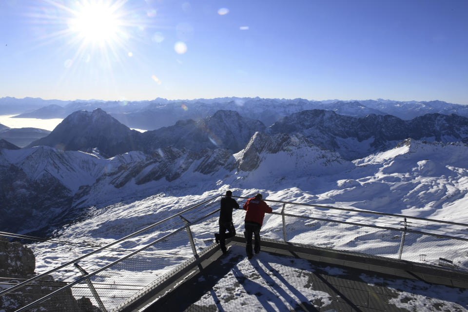 Two employees look out over the closed ski resort at the Zugspitze in Grainau, Germany, Monday, Nov 30, 2020. The skiing areas are prepared but due to the Corona pandemic restrictions skiing is not allowed at the area. (Angelika Warmuth/dpa via AP)