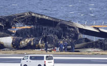 Police investigator look at the burn-out wreckage of Japan Airlines plane at Haneda airport on Thursday, Jan. 4, 2024, in Tokyo, Japan. A transcript of communication between traffic control and two aircraft that collided and burst into flames at Tokyo’s Haneda Airport showed that only the larger Japan Airlines passenger flight was given permission to use the runway where a coast guard plane was preparing for takeoff. (Kyodo News via AP)