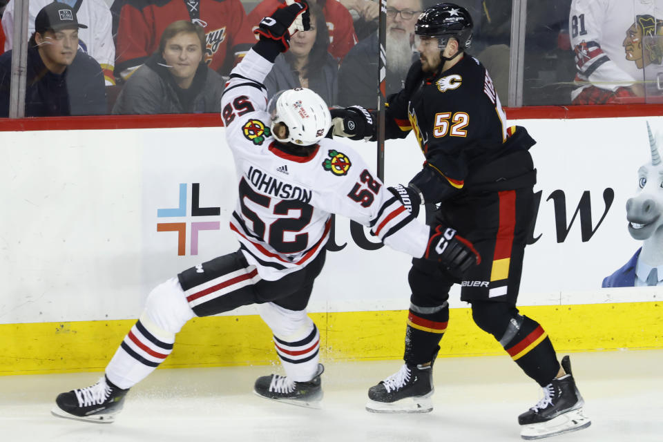 Chicago Blackhawks' Reese Johnson, left, is knocked down by Calgary Flames' MacKenzie Weegar during the first period of an NHL hockey game Saturday, Jan. 27, 2024, in Calgary, Alberta. (Larry MacDougal/The Canadian Press via AP)