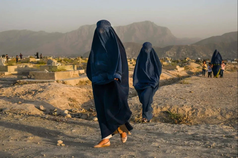 Afghan women wearing traditional burqas walk past a cemetery in Kabul (AFP via Getty Images)