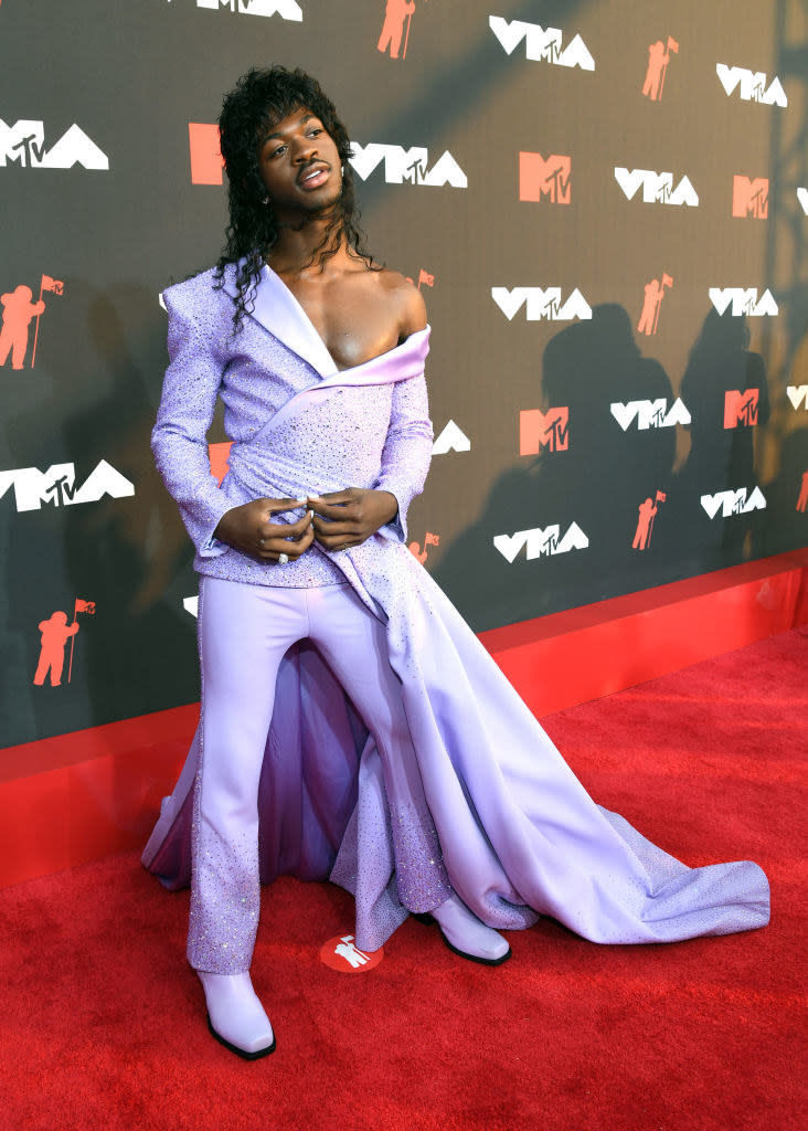 Lil Nas X wears a brightly colored off the shoulder blazer and matching pants with a train tied around his waist