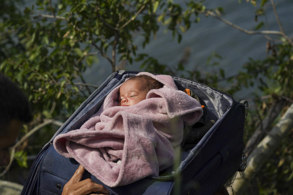 Migrantes cruzan el río Bravo hacia Estados Unidos con un bebé dentro de una maleta abierta, en esta fotografía tomada desde Matamoros, México, el miércoles 10 de mayo de 2023. (AP Foto/Fernando Llano)