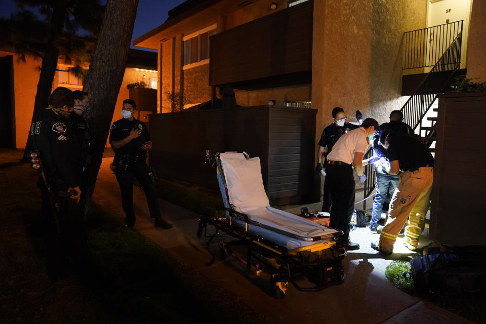 A police officer shines a flashlight as emergency medical workers Trenton Amaro, far right, and Joshua Hammond, second from right, check the vitals of a handcuffed patient in Placentia, Calif., Saturday, Jan. 9, 2021. EMTs and paramedics have always dealt with life and death — they make split-second decisions about patient care, which hospital to race to, the best and fastest way to save someone — and now they're just a breath away from becoming the patient themselves. (AP Photo/Jae C. Hong)