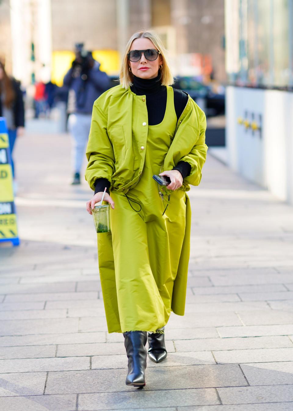 Kristen Bell in a neon green coat and black boots walking down the street