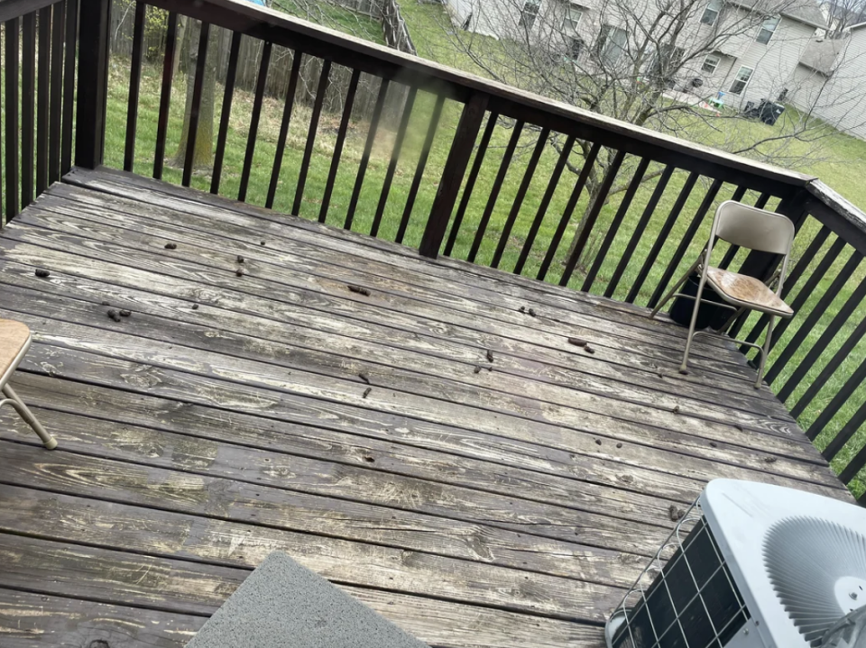 Wooden deck with two chairs and an air conditioning unit, overlooking a backyard