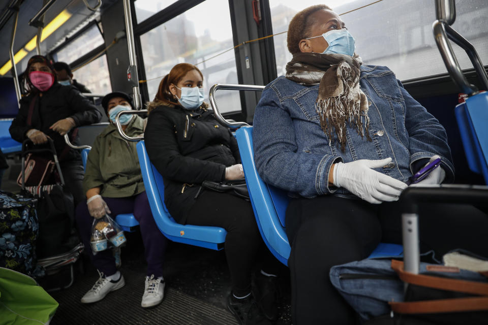 In this Thursday, April 23, 2020 photo, Ruth Caballero, a nurse with The Visiting Nurse Service of New York, right, and Catherine Peralta, her Spanish-language translator, center, ride a bus to a patient's home during their rounds in upper Manhattan in New York. Home care nurses, aides and attendants, who normally help an estimated 12 million Americans with everything from bathing to IV medications, are now taking on the difficult and potentially dangerous task of caring for coronavirus patients. (AP Photo/John Minchillo)