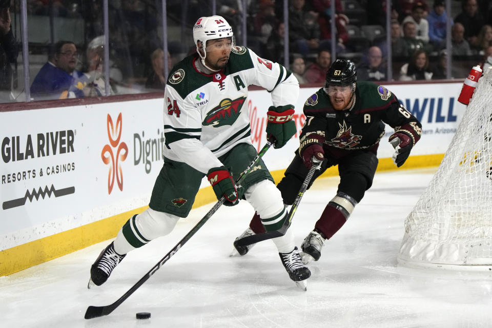 Minnesota Wild defenseman Matt Dumba (24) carries the puck in front of Arizona Coyotes left wing Lawson Crouse in the first period during an NHL hockey game, Monday, Feb. 6, 2023, in Tempe, Ariz. (AP Photo/Rick Scuteri)