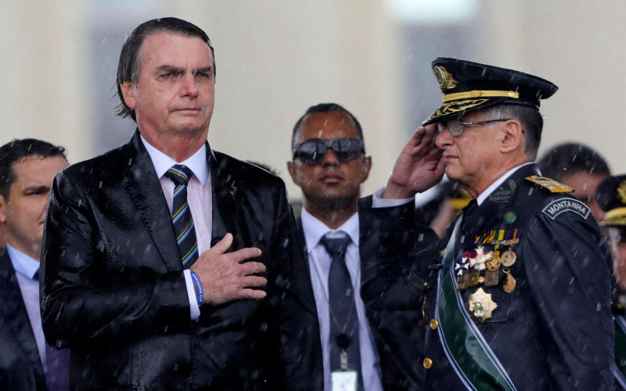 Jair Bolsonaro (L) and Army Commander Edson Pujol are drenched with rain as they attend a ceremony to mark Army Day in 2019 - AFP