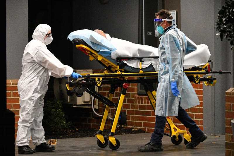 Healthcare workers transport a person into a patient transport vehicle at the Arcare Aged Care facility in Melbourne.