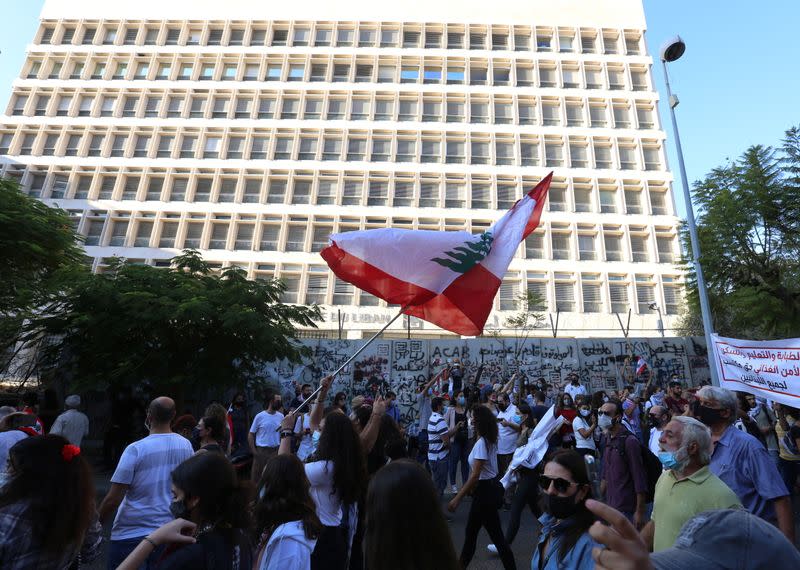 An anti-government demonstrator holds a Lebanese flag during a protest as Lebanese mark one year since the start of nation-wide protests, in front of the central bank building in Beirut