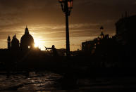 In this photo taken on Sunday, Nov. 17, 2019, a gondolier is silhouetted in a golden sunset in Venice, Italy. Venetians are fed up with what they see as an inadequate to the city's mounting problems: record-breaking flooding, damaging cruise ship traffic and over-tourism. They feel largely left to their own devices, and with ever fewer Venetians living in the historic part of the city to defend its interests and keep it from becoming a theme park or museum. (AP Photo/Luca Bruno)