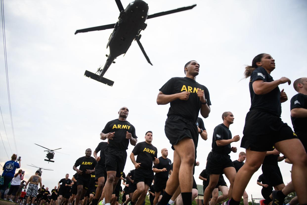 A Blackhawk flies over as soldiers run in the 82nd Airborne Division run on Fort Liberty.