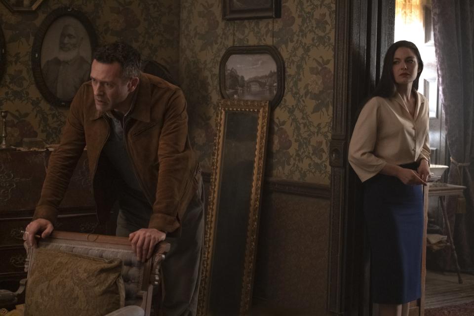 In a still from The Man in the High Castle, a man leans on a chair and a woman looks at him from a doorway