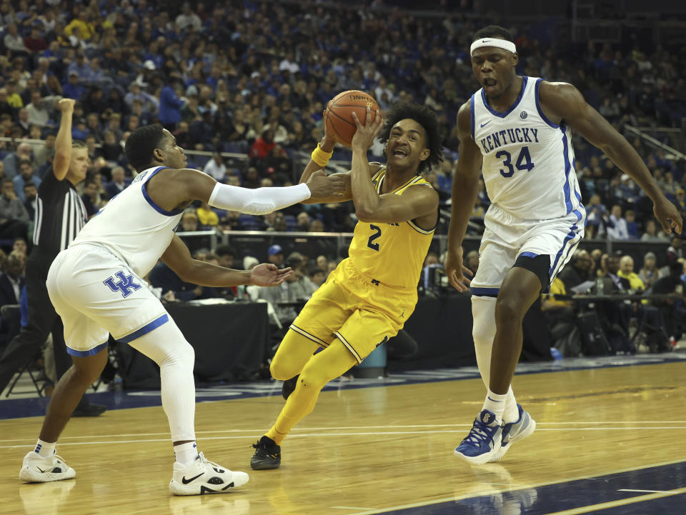 Michigan Wolverines' Kobe Bufkin (2) goes for the basket as Kentucky Wildcats' Sahvir Wheeler (2), left, and Kentucky Wildcats' Oscar Tshiebwe (34) defend during an NCAA basketball game between Michigan Wolverines and Kentucky Wildcats at the O2 Arena, in London, Sunday, Dec.4, 2022. (AP Photo/Ian Walton)