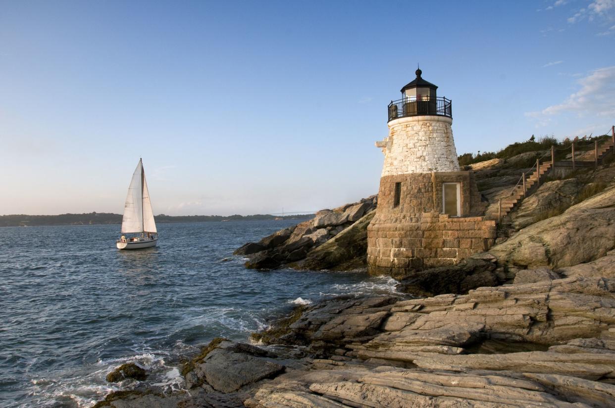 Lighthouse in the cliffs next to the sea with a sailboat sailing by.