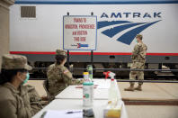 Members of the Rhode Island National Guard look for passengers getting off a train from New York as it arrives Saturday, March 28, 2020, in Westerly, R.I. States are pulling back the welcome mat for travelers from the New York area, which is the epicenter of the country's coronavirus outbreak, and some say at least one state's measures are unconstitutional. Gov. Gina Raimondo ratcheted up the measures announcing she'll also order the state National Guard to go door-to-door in coastal communities starting this weekend to find out whether any of the home's residents have recently arrived from New York and inform them of the quarantine order. (AP Photo/David Goldman)