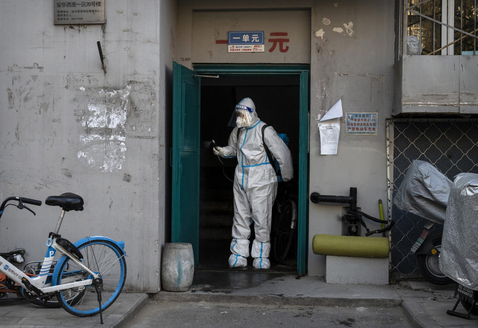 An epidemic control worker wears PPE as he disinfects a doorway in a neighborhood that recently was in lockdown due to COVID-19 cases and has now opened (Kevin Frayer / Getty Images)